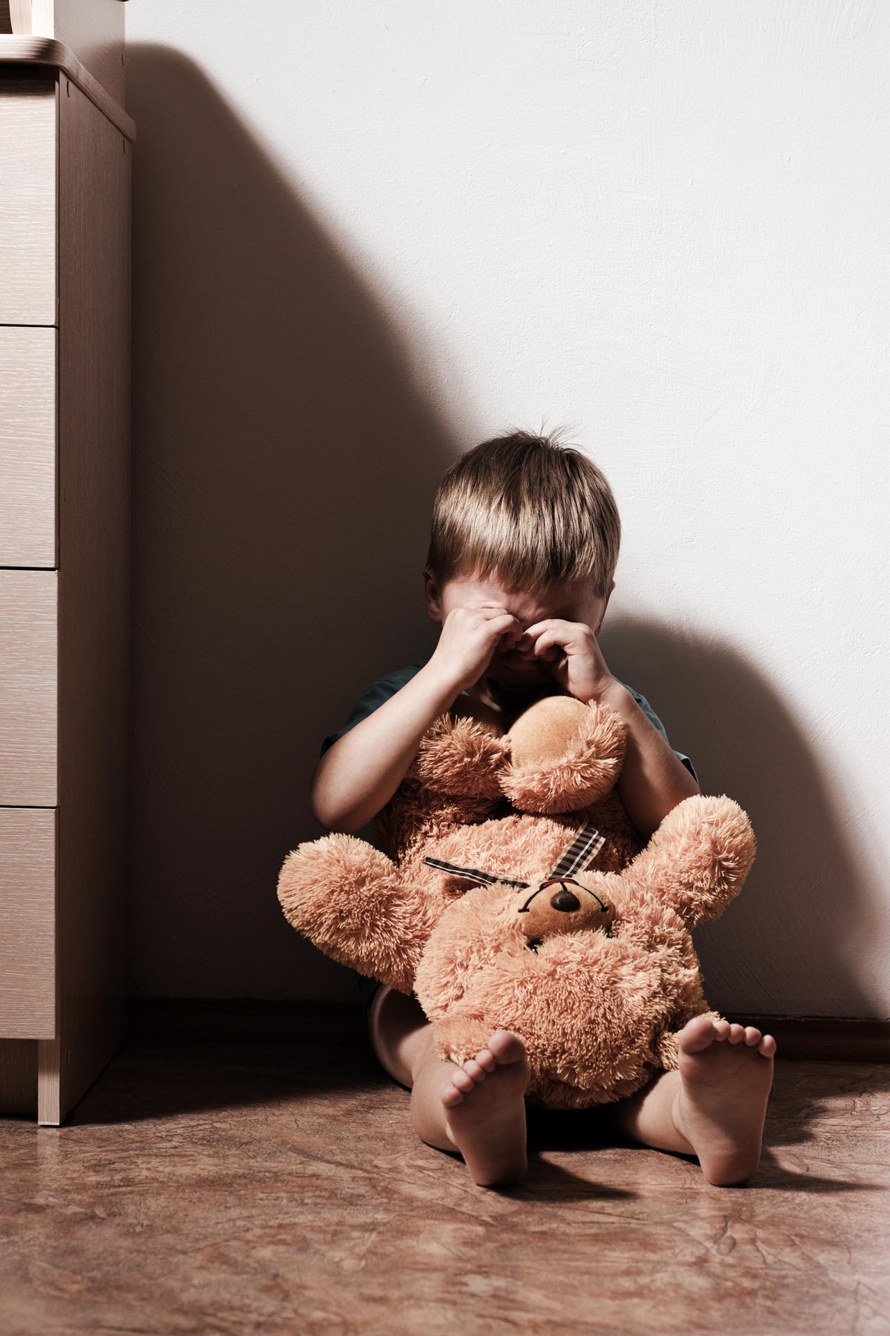 Kind weint mit Teddybär im Zimmer